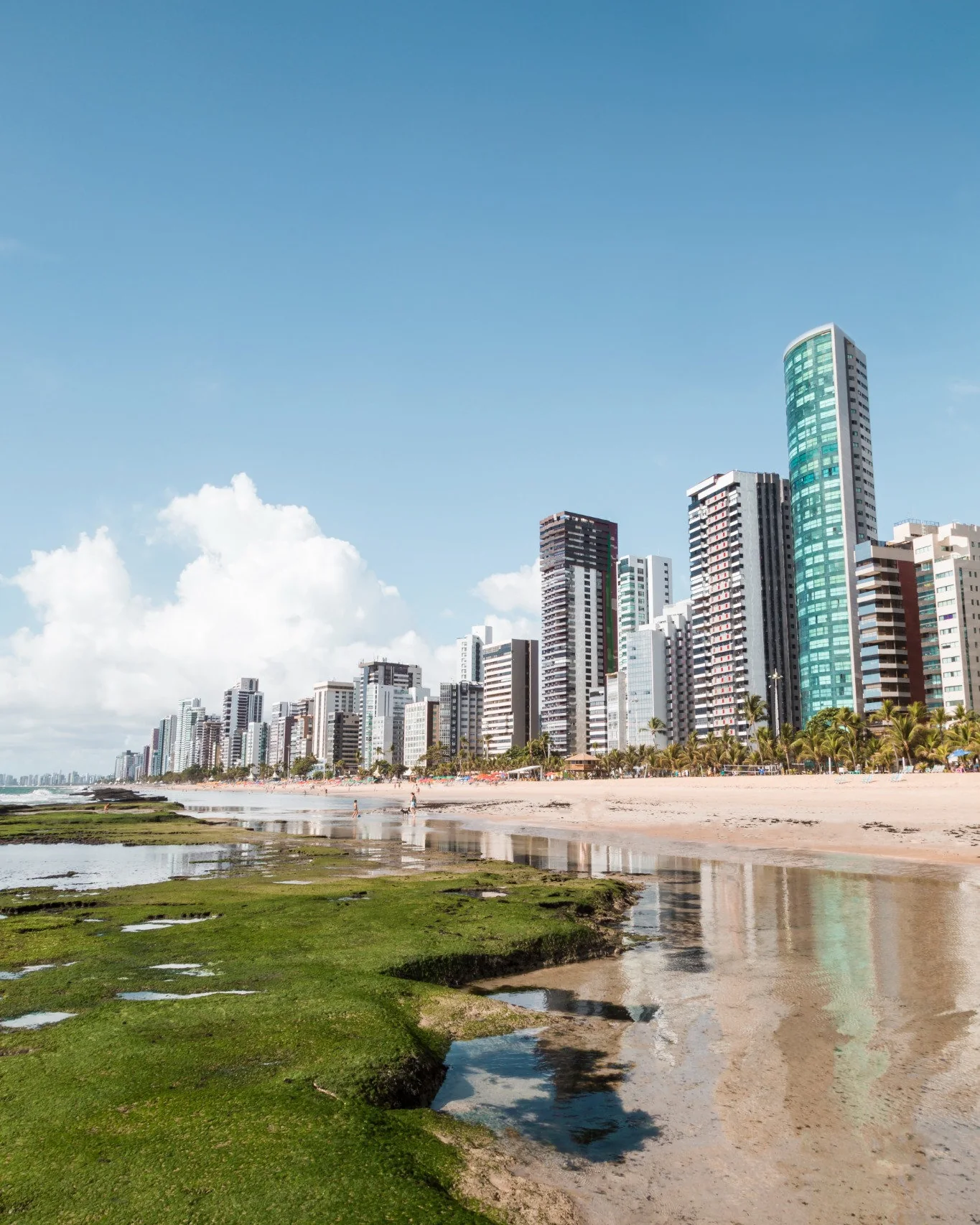 Orla de Boa Viagem, no Recife, com prédios à beira mar e piscinas naturais na maré baixa.