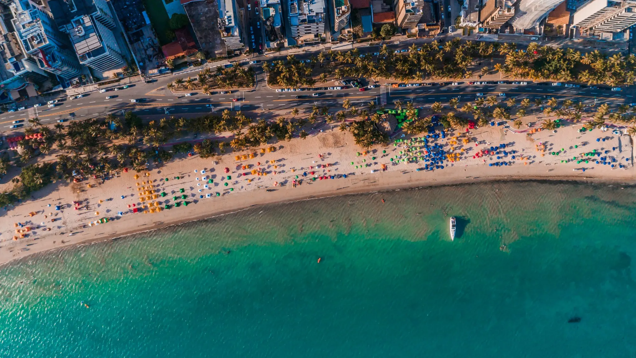 Praia de água turquesa com guarda-sóis coloridos em Maceió, Alagoas, vista do alto.